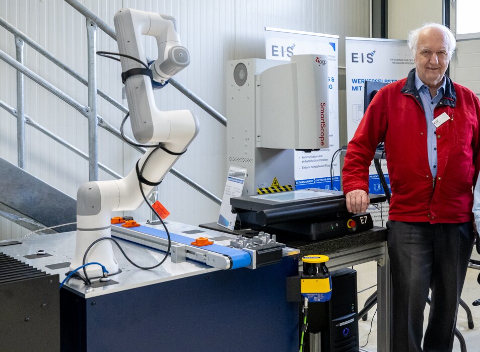 Unser Messtechnik-Partner Herr Lenz neben einer automatisierten OGP-SmartScope-Messzelle mit Cobot und Förderband